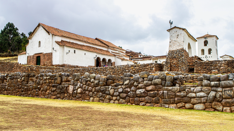 View of the Chinchero ruins with lush green terraces and mountain peaks in the background during the dry season